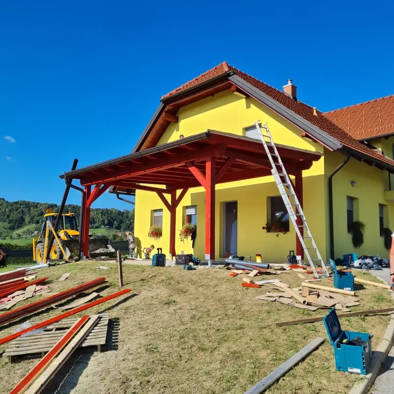 Montaža lesenega nadstreška z rdeče lakiranimi stebri pred hišo
