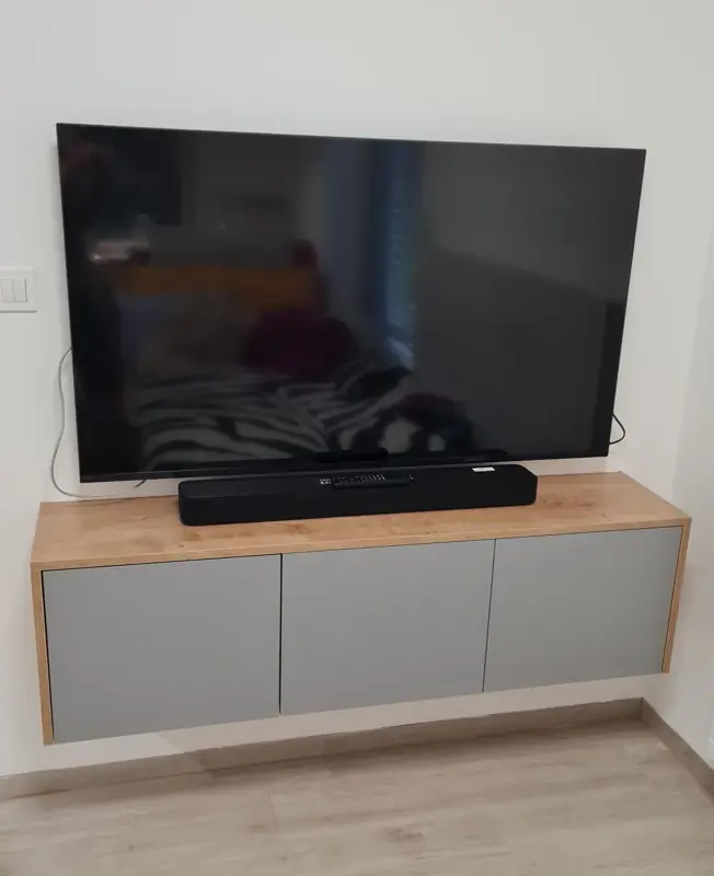 Viseča TV omarica s hrastovo ploščo in sivimi fronti pod stenskim televizorjem